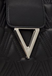 Black leather bag with a quilted texture, featuring a triangular silver metal clasp. Accentuated by geometric stitch patterns.