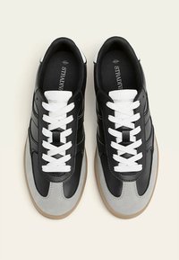 Baskets noires et grises avec lacets blancs. Matériaux en cuir et en daim, forme arrondie, cheville rembourrée et semelle extérieure en gomme texturée.