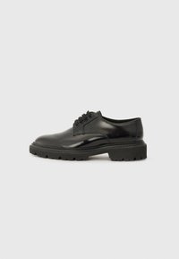 Chaussure noire en cuir à lacets avec une finition lisse, un bout arrondi et une semelle en caoutchouc épaisse avec un motif de semelle texturé.