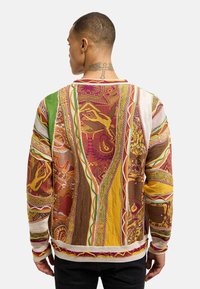 Pull en tricot avec un motif multicolore et des teintes riches de rouge, jaune, vert et marron. Tissu texturé avec des poignets côtelés.