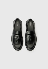 Black leather loafers with a smooth finish, featuring a wide strap and decorative hardware. Rounded toe and textured sole for grip.