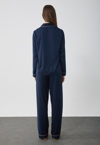 Mörkblå pyjamasset i mjukt tyg, med långärmad skjorta med krage och matchande byxor med kontrasterande kant vid ärmsluten.