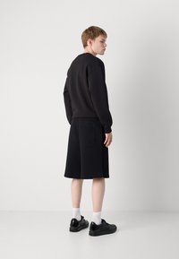 Black sweatshirt with dropped shoulders, paired with black shorts featuring an elastic waistband and back pocket. Black sneakers with white socks.