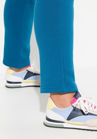 Teal svettbyxor med uppvikta fållar, ihop med flerfärgad sneakers med vita, blå, rosa och gula detaljer, strukturerad tyg och en synlig logotyp.