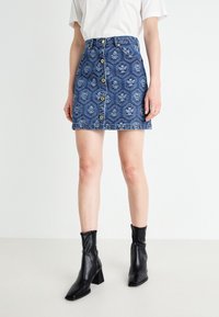 Denim mini skirt with floral patterns and front buttons worn with black ankle boots and a white short-sleeve top.
