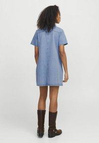 Trumpas džinsinis suknelė su trumpomis rankovėmis, šviesiai mėlynos spalvos ir tiesaus kirpimo. Dėvima su iki kelių siekiančiais rudo odinio batų. Paprasti siuvimo detalės.