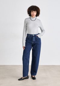 Gray long-sleeve top with high collar, paired with high-waisted dark blue denim jeans. Black flat shoes, simple design, minimalist aesthetic.
