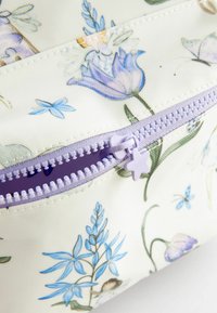 Pungă zip florală cu un fundal alb, având flori violet și albastre. Fermoul este de lavandă cu un detaliu în formă de stea. Material texturat.