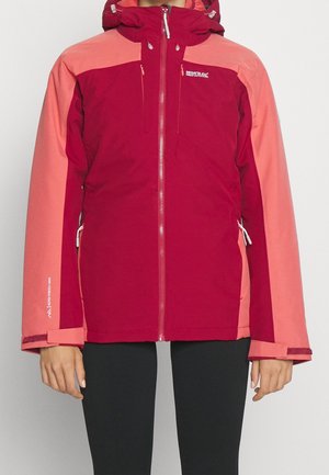 Dwukolorowa, czerwona i różowa kurtka outdoorowa z przednim zamkiem błyskawicznym, zamykanymi na zamek kieszeniami na piersi i po bokach oraz regulowanymi paskami na nadgarstkach na osobie noszącej czarne spodnie.