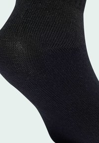 Calzino in cotone nero con texture a coste, forma aderente e finitura liscia. L'immagine si concentra sulla zona della caviglia, evidenziando il motivo del tessuto.