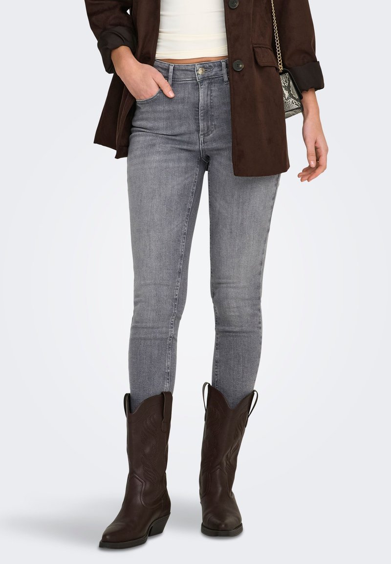 Grijze skinny jeans met een mid-rise pasvorm, gemaakt van denim, gecombineerd met bruine cowboylaarzen en een donkerbruine suède jas.