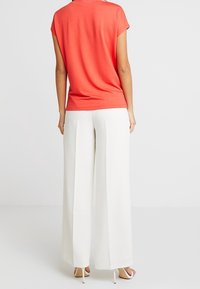 Top coral de manga corta combinado con pantalones blancos de pierna ancha. Textura suave, ajuste entallado, con una silueta relajada. Diseño simple sin patrones.