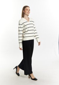 Maglione a maglia crema con righe nere, scollo a V e maniche lunghe abbinato a pantaloni neri a gamba larga e scarpe con tacco nere.