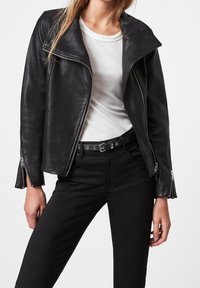 Svart läderbikerjacka med bred krage, dragkedja fram och långa ärmar. I kombination med svarta åtsittande jeans och en vit undertröja.