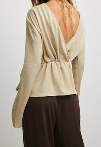 Top beige a maniche lunghe con scollatura a V profonda, vita arricciata e tessuto morbido e liscio. Il design drappeggiato crea una silhouette rilassata.