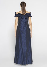 Granatowa sukienka bez ramiączek z falbaniastym dekoltem i dopasowanym gorsetem, zwiewną spódnicą oraz gładkim, błyszczącym materiałem. Posiada ukryty zamek z tyłu.