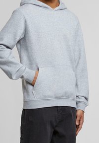 Sudadera con capucha de color gris claro, confeccionada en una tela suave, con un bolsillo frontal, puños y dobladillo de canalé, y un corte casual.