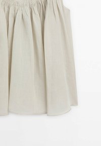 Jupe en tissu froncé beige clair avec une silhouette ample et fluide et une texture douce sur fond blanc.
