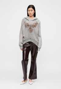 Γκρι φούτερ με κουκούλα, σχέδιο αετού, μακριά μανίκια και κορδόνι στην κουκούλα· συνδυασμένο με λαμπερό, σκούρο καφέ παντελόνι κανονικής γραμμής.