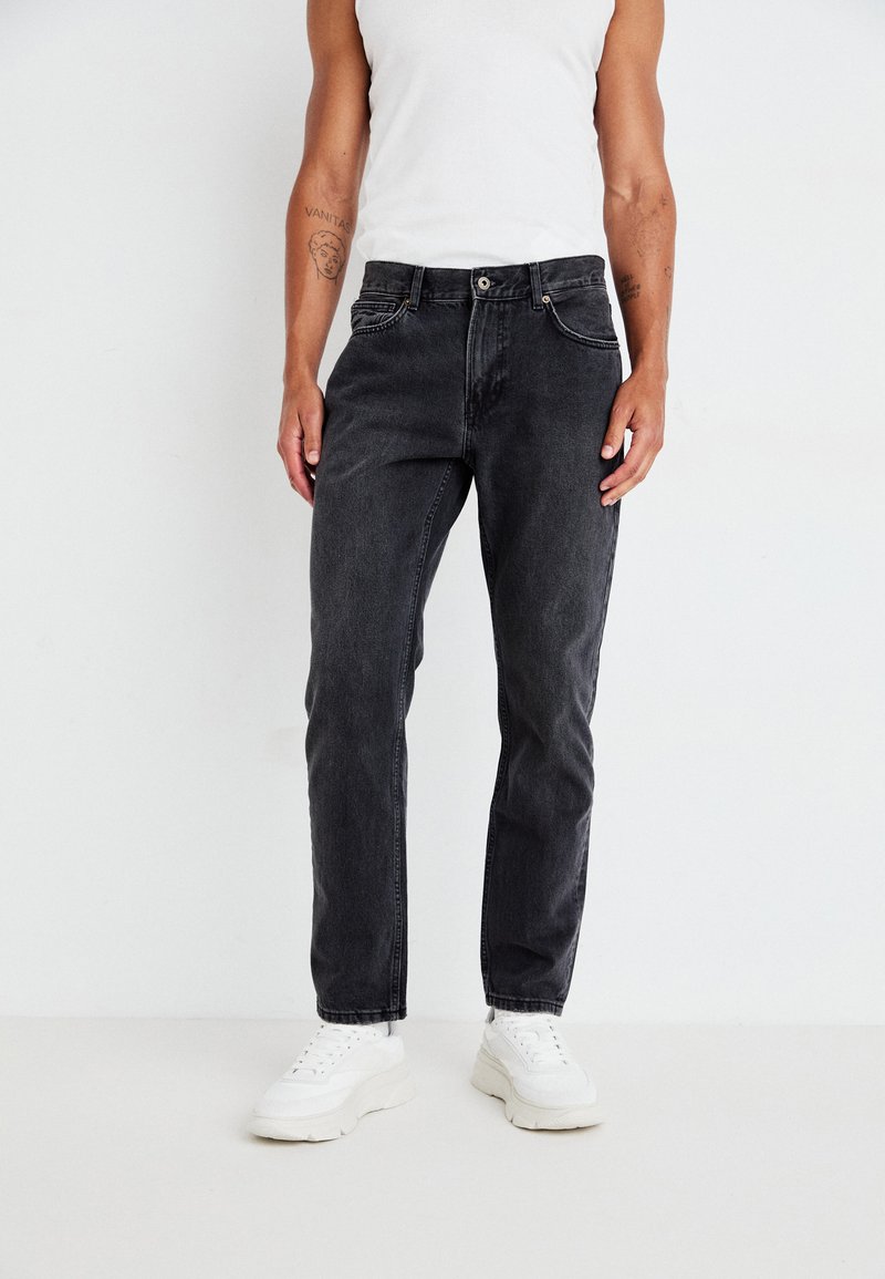 Zwarte denim jeans met een rechte pasvorm, vijf zakken en een subtiele vervaging. Gestyled met een witte tanktop en witte sneakers.
