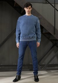 Sudadera de cuello redondo de mezclilla en azul claro con puños y dobladillo acanalados, combinada con jeans ajustados azul oscuro y botas negras con hebilla.