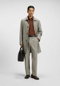 Grå rutig kappa över brun polo, matchat med byxor och mörka skor. Håller en mörk läderväska med en slät yta och rena linjer.