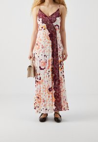 Sukienka maxi w białym kolorze z kwiatowym wzorem w odcieniach pomarańczowego i burgundowego, z koronkowym wykończeniem z przodu. Cienkie ramiączka i luźny materiał.