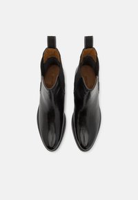 Botines de cuero negro con acabado brillante, paneles laterales elásticos, lengüetas y un interior suave. Punta redondeada y tacón bajo.
