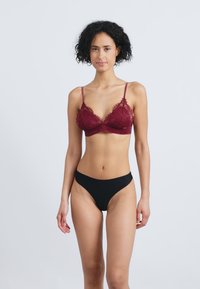 Bralette de encaje burdeos con tirantes finos, combinado con bragas de bikini de corte alto en negro. El bralette presenta un delicado patrón floral y bordes ondulados.