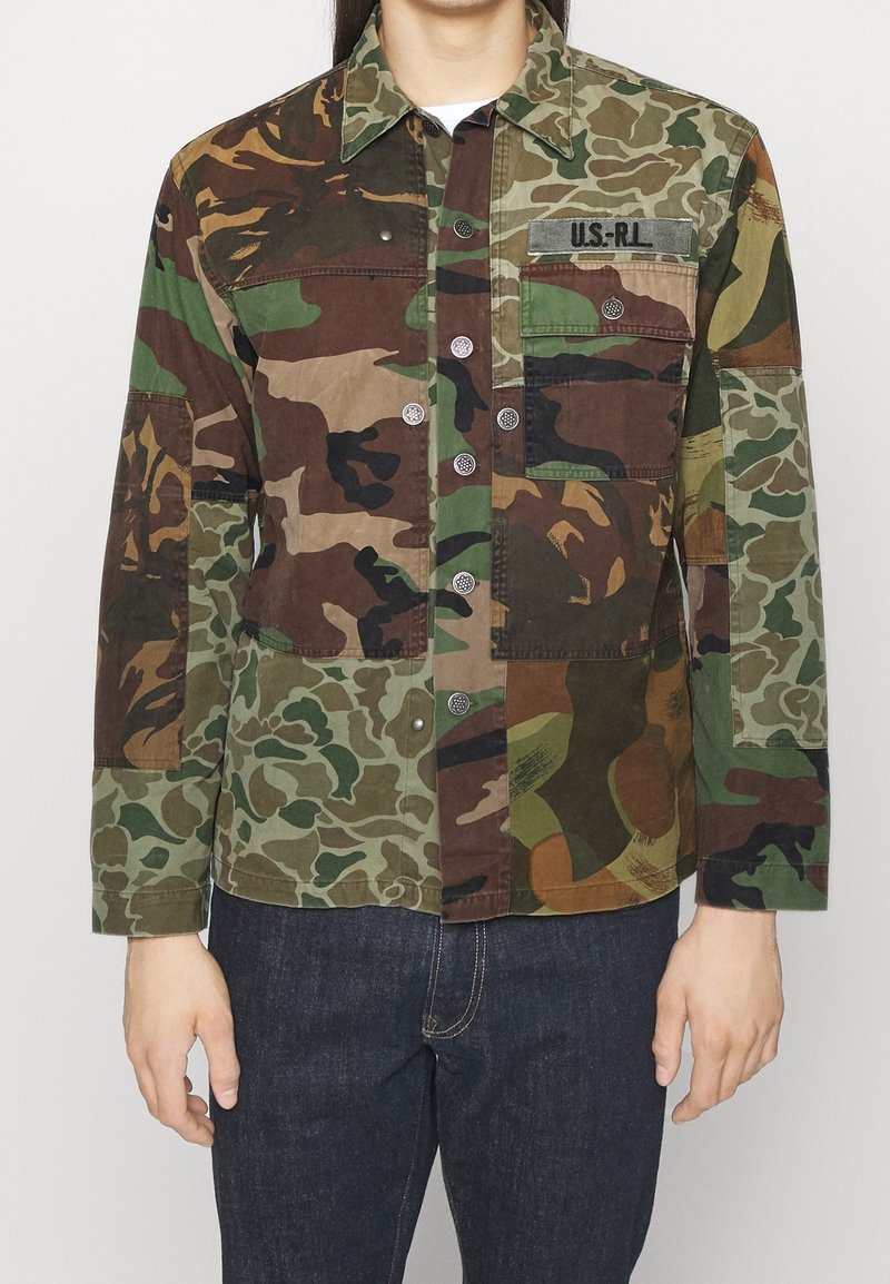 Bunda s camouflage vzorem v různých odstínech zelené, hnědé a béžové. Má patentní knoflíky, náprsní kapsu a uvolněný střih.