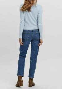 Světlomodrý top s dlouhým rukávem, spárovaný s tmavomodrými džíny s vysokým pasem. Hnědé kotníkové boty na podpatku. Zadní pohled, hladká textura a přiléhavý střih.