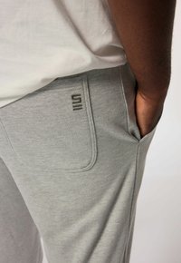 Grijze joggingsbroeken gemaakt van zachte stof, met een achterzak met een geborduurd logo en een relaxte pasvorm. Zijhandzakken zichtbaar.