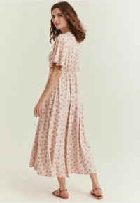 Lång rosa blommig klänning med korta fladderärmar, figursydd midja och en flödande kjol. Har ett litet blommönster och lättviktsmaterial.