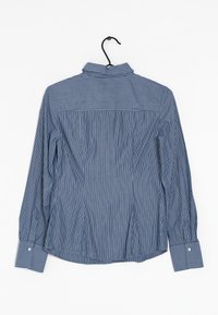 Camisa de manga larga a rayas azul y blanca con cuello, puños abotonados y un diseño de pliegues en la parte posterior. Fabricada en tela ligera. Cuélga de un gancho negro.
