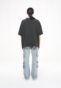 Přesně padnoucí černé bavlněné tričko s krátkým rukávem, kombinované se světle modrými cargo kalhotami s několika bočními kapsami a rozšířeným střihem.