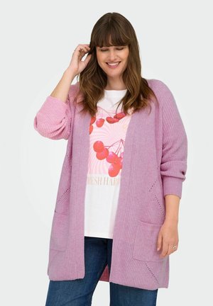 Lichtroze cardigan met ribbelstructuur, open voorkant, twee zakken en middelmatige mouwlengte, gedragen over een witte graphic t-shirt en donkere jeans.