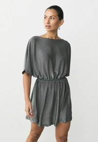 Rochie lucioasă, cu mânecă scurtă, de culoare gri închis, cu un brâu elastic. Confecționată dintr-un material moale, ușor, cu un efect subtil de strălucire.