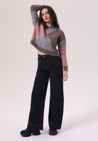 Pull en crochet dans des tons de gris et de rose avec un design court, associé à un jean noir taille haute à jambe large et des baskets noires.