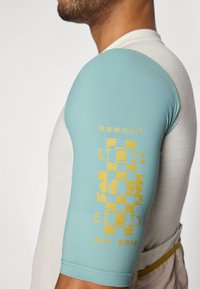 T-shirt de sport gris clair et turquoise avec une texture côtelée ; présente un logo Oakley jaune et un design graphique sur la manche turquoise.