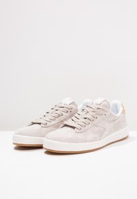 Jasnoszare zamszowe trampki z białymi detalami, okrągłym noskiem, sznurowanym zapięciem i gumową podeszwą. Posiadają perforowane zdobienia po bokach.