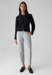 Gilet noir à côtes avec un col, fermeture à boutons et poche avant, associé à un pantalon tapered gris clair et des mocassins noirs.