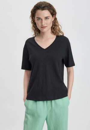 Zwarte V-hals t-shirt van zacht materiaal, met korte mouwen en een relaxte pasvorm, gecombineerd met muntgroene broek.