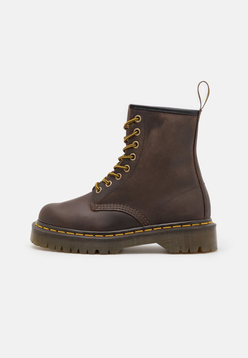 Botte en cuir brun foncé à lacets avec semelle en caoutchouc épaisse, coutures jaunes et languette à l'arrière, vue de profil.
