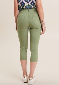 Pantaloni verdi a cropped realizzati in tessuto elasticizzato, dotati di due tasche posteriori, una vita alta e una vestibilità slim. Indossati con sneakers bianche.