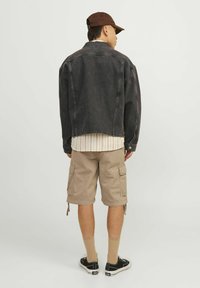 Sort denimjakke, beige cargo shorts, brun kasket, tan strømper, sorte sneakers. Stribet skjorte synlig ved taljen. Casual outfit set bagfra.