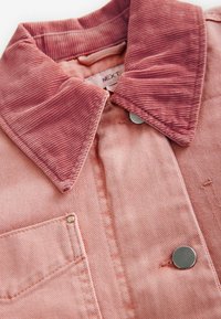 Lys pink cordjakke med tekstureret krave, sølvdetaljer og en brystlomme med knap. Rene linjer og syninger.
