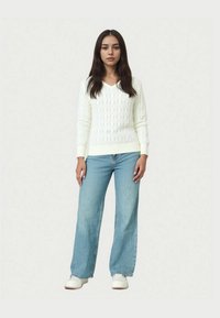 Pulover alb cu model tip torsadă și decolteu în V, asortat cu blugi largi de culoare bleu deschis. Mâneci și talie cu manșete canelate, textură netedă, croială casual.