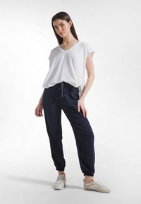 Camiseta blanca de cuello en V con mangas cortas combinada con pantalones jogger azul marino. Los pantalones tienen una cinturilla elástica y puños en los tobillos recogidos.