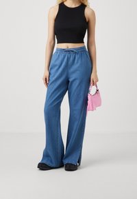 Blue wide-leg denim pants with an elastic waistband, paired with a black sleeveless top and a small pink handbag. Black sneakers complete the look.
