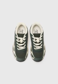 Zielone siateczkowe i syntetyczne sneakersy z kremowymi sznurówkami, zaokrąglonym noskiem oraz wzorzystymi akcentami po bokach. Gruba czarna gumowa podeszwa.